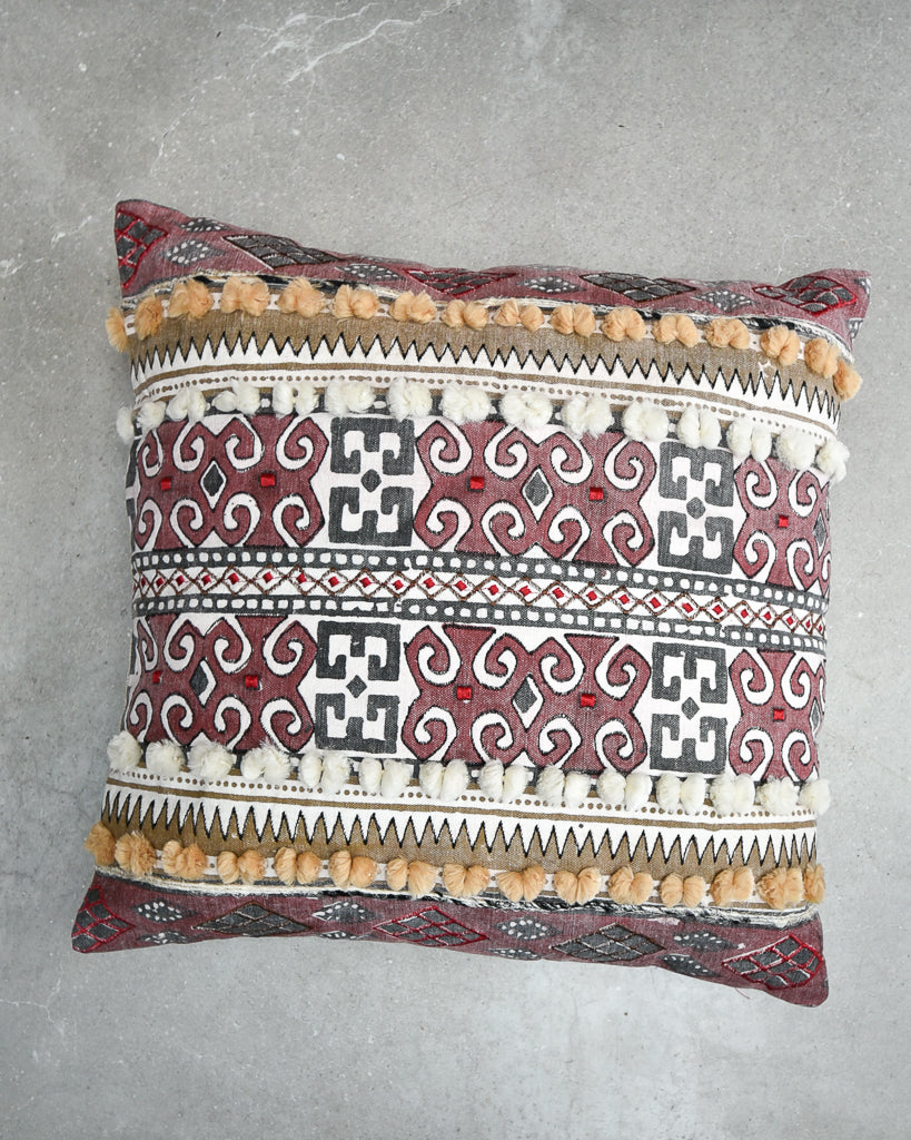 Decorative pillow with geometric pattern and pom-pom trim on a gray background