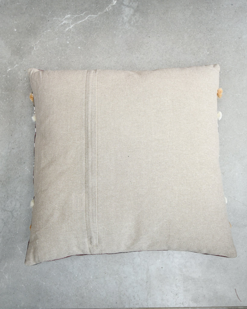 Beige pillow with pom-pom trim on a gray surface