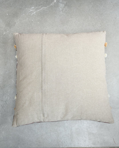 Beige pillow with pom-pom trim on a gray surface