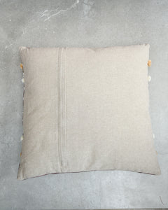 Beige pillow with pom-pom trim on a gray surface