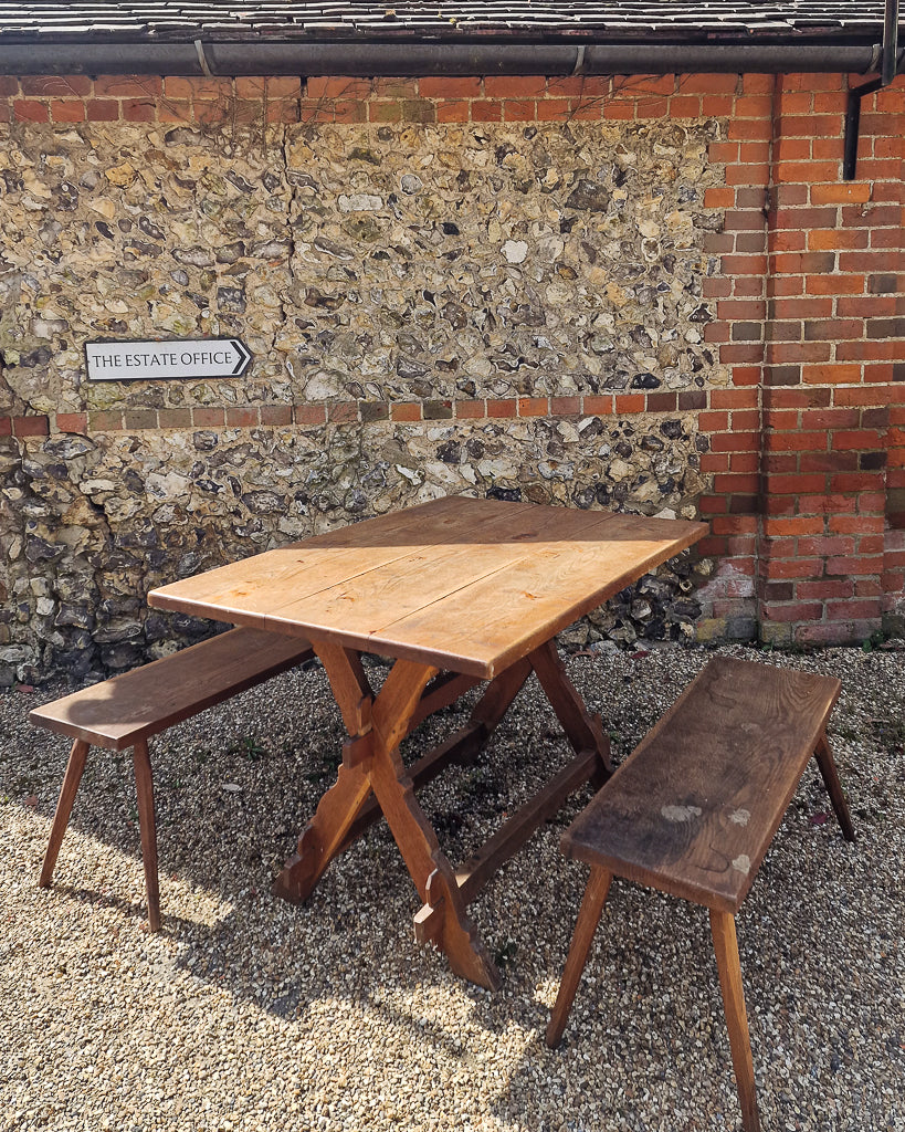 German solid oak dining table with three plank top and trestle base, paired with rustic wooden benches in farmhouse setting