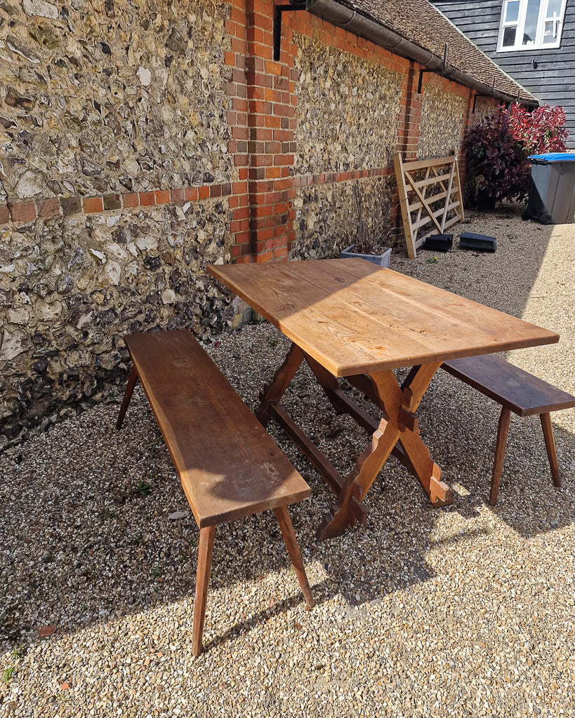 German solid oak dining table with three plank top and trestle base, paired with rustic wooden benches in farmhouse setting